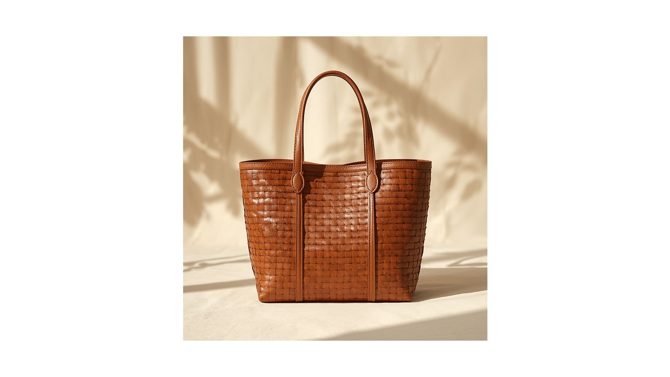 Woven leather tote bag in a rich cognac shade. Handcrafted basket-style handbag with slim leather handles, perfect for a coastal 2026 summer wardrobe or professional travel.