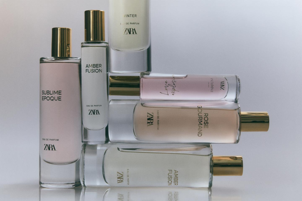 A bottle of Zara Emotions perfume (Ebony Wood) with a white label and black cap, set against a blurred background of white flowers and green leaves in soft, natural daylight.