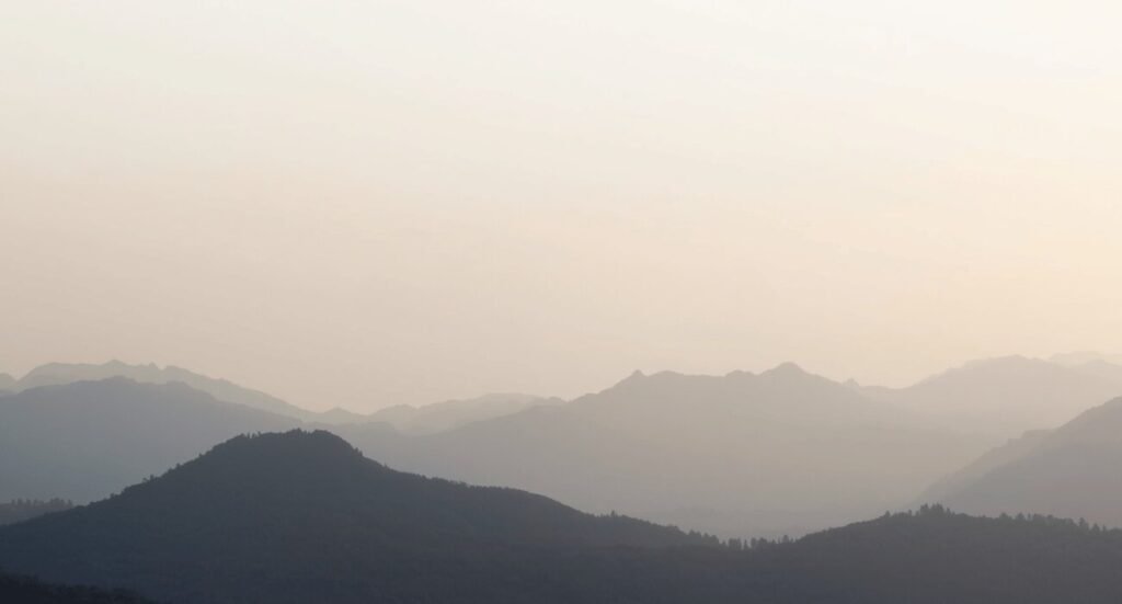Minimalist misty mountain layers shrouded in soft fog under a muted beige sky aesthetic wallpaper.